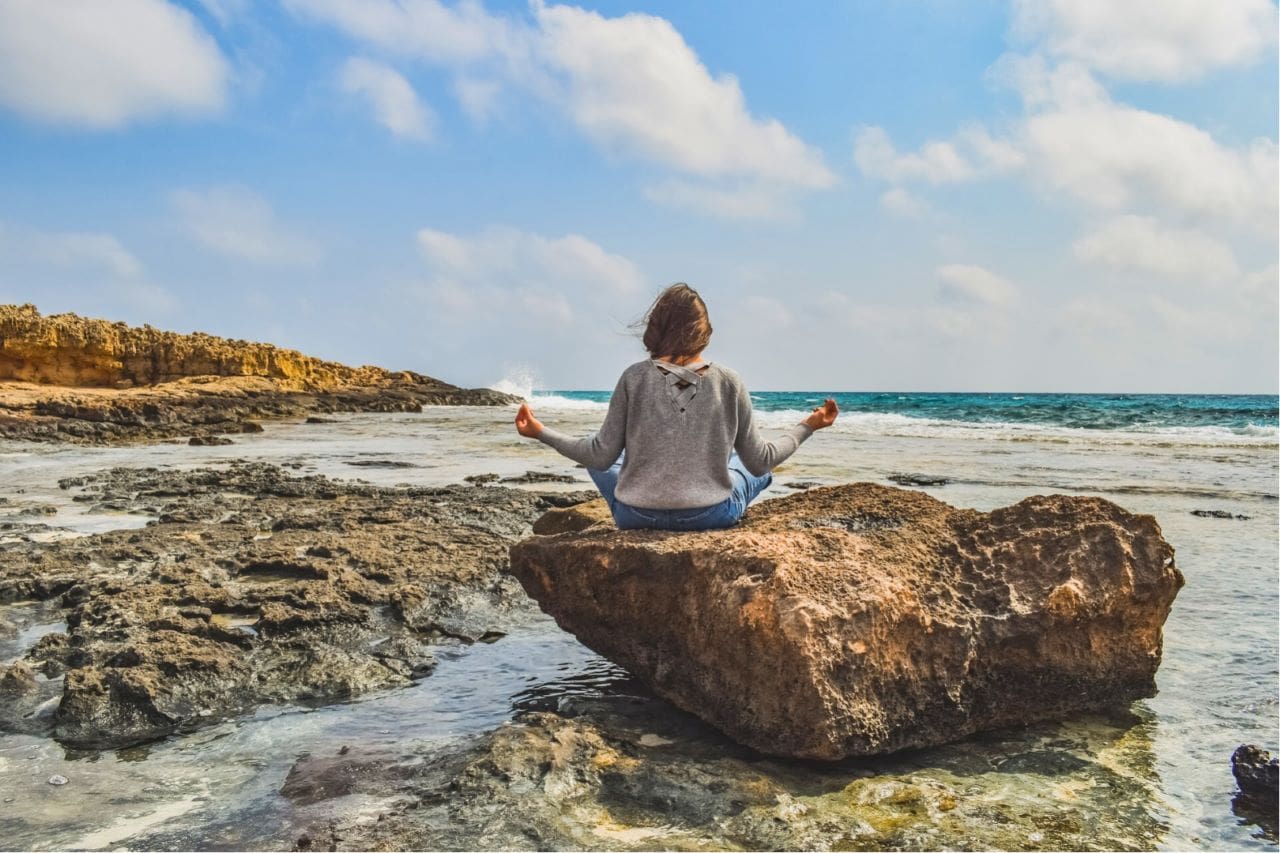 A person sitting on top of a rock in the ocean.